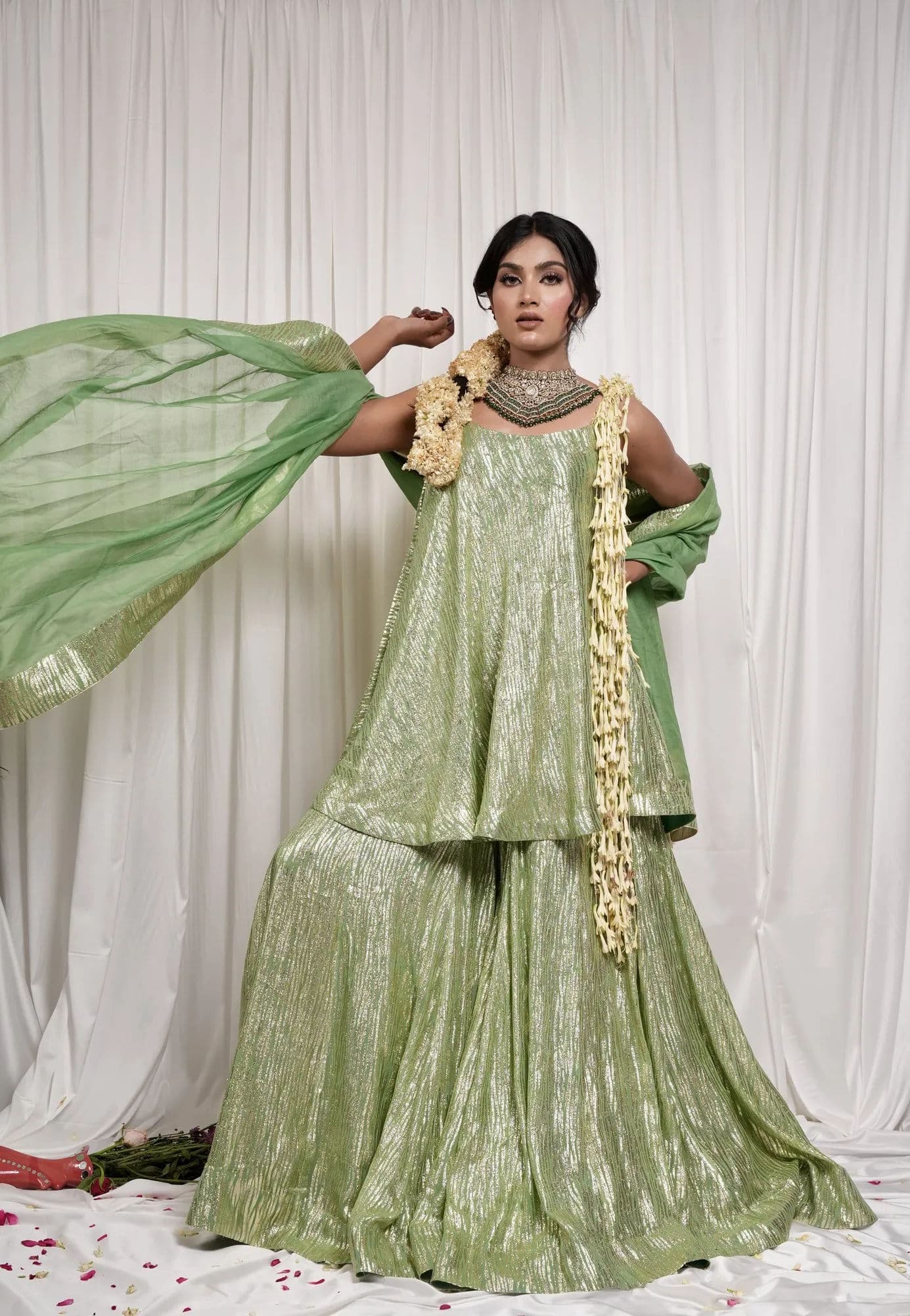 A sage green brocade sharara with the dupatta caught mid-air.